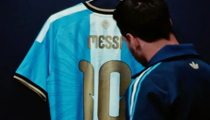 Lionel Messi mirando la camiseta especial celeste con detalles dorados y el Sol de Mayo en la espalda, para su último partido con Argentina