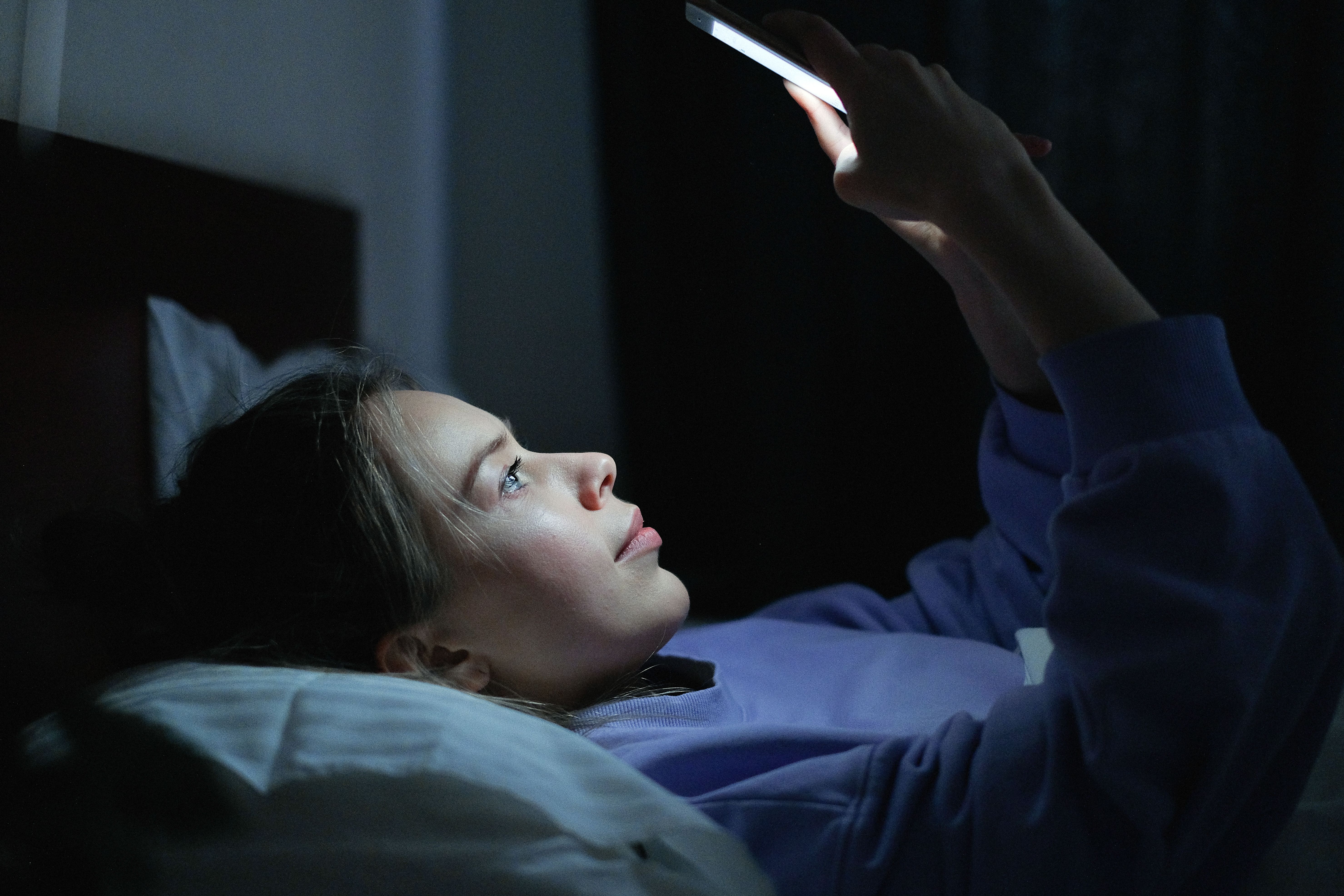 Image of a person scrolling through phone on dark room at night