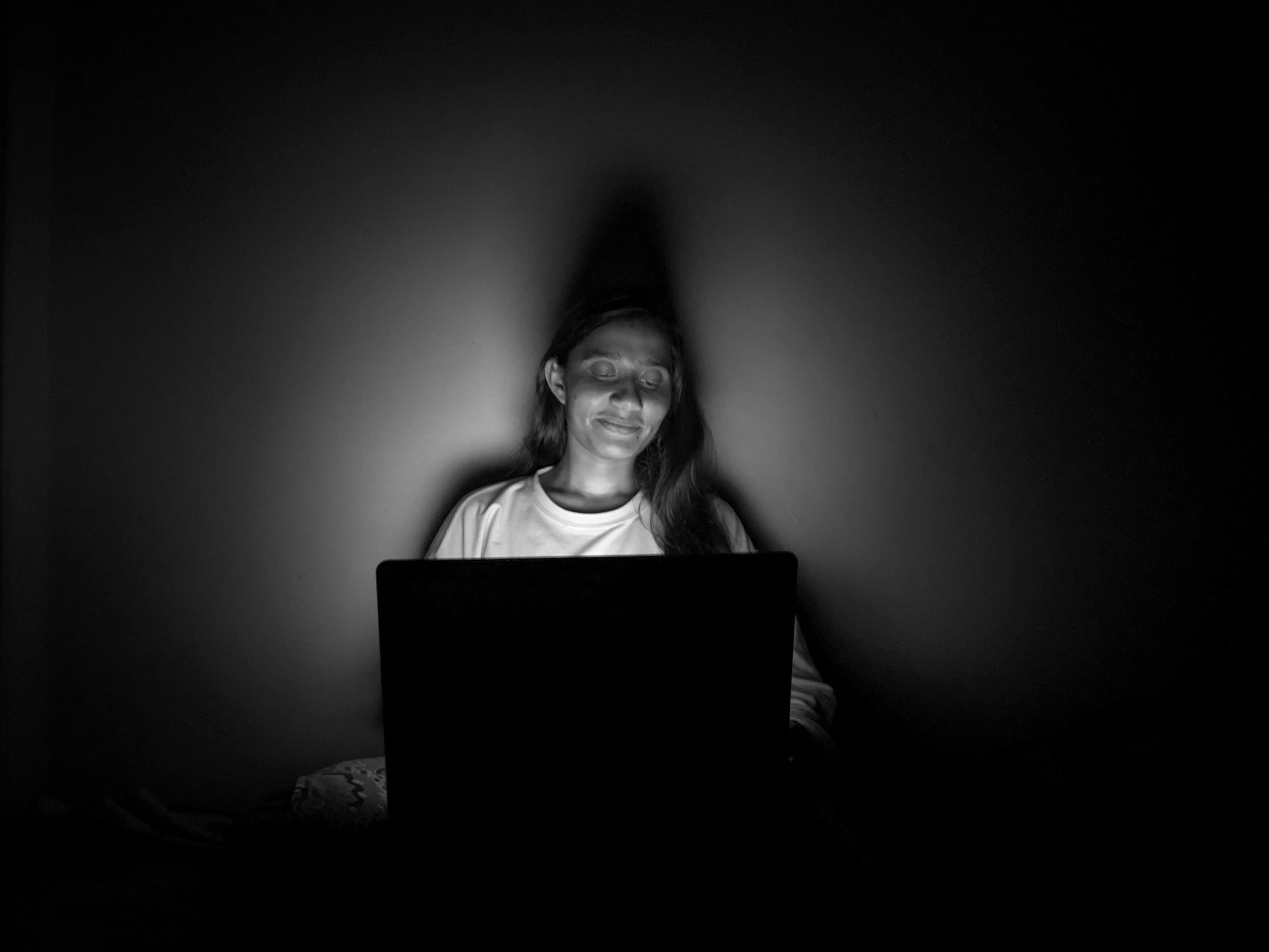 Woman sitting in a dark room illuminated by a laptop screen, creating a serene ambiance