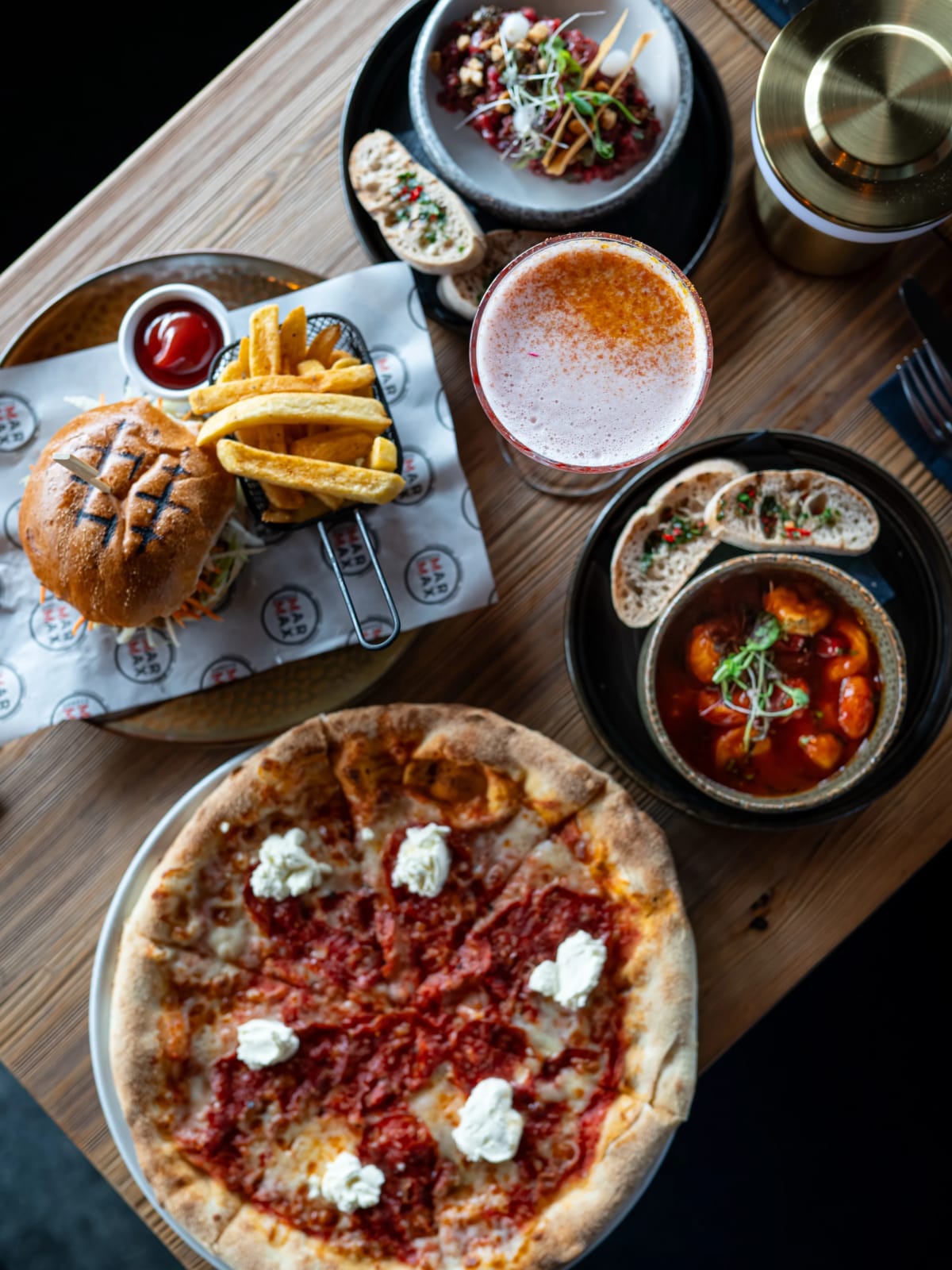 Pizza, burger z frytkami i przystawki z menu Riverside na jednym stole
