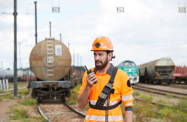 Employé vue de face parlant dans un talkie-walkie aavec en fond des trains