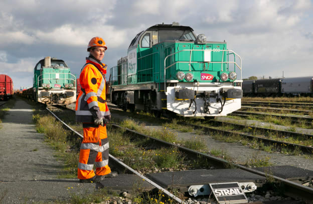 Une employée sur des rails avec derrière un train