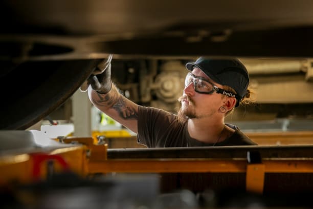 Opérateur de maintenance portant des lunettes et une casquette réalisant un contrôle des essieux
