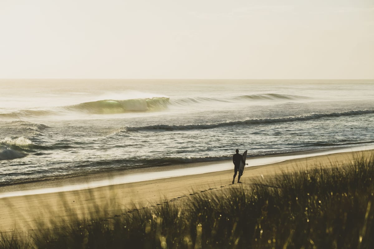 Surfer walking along a King Island beach at sunset
