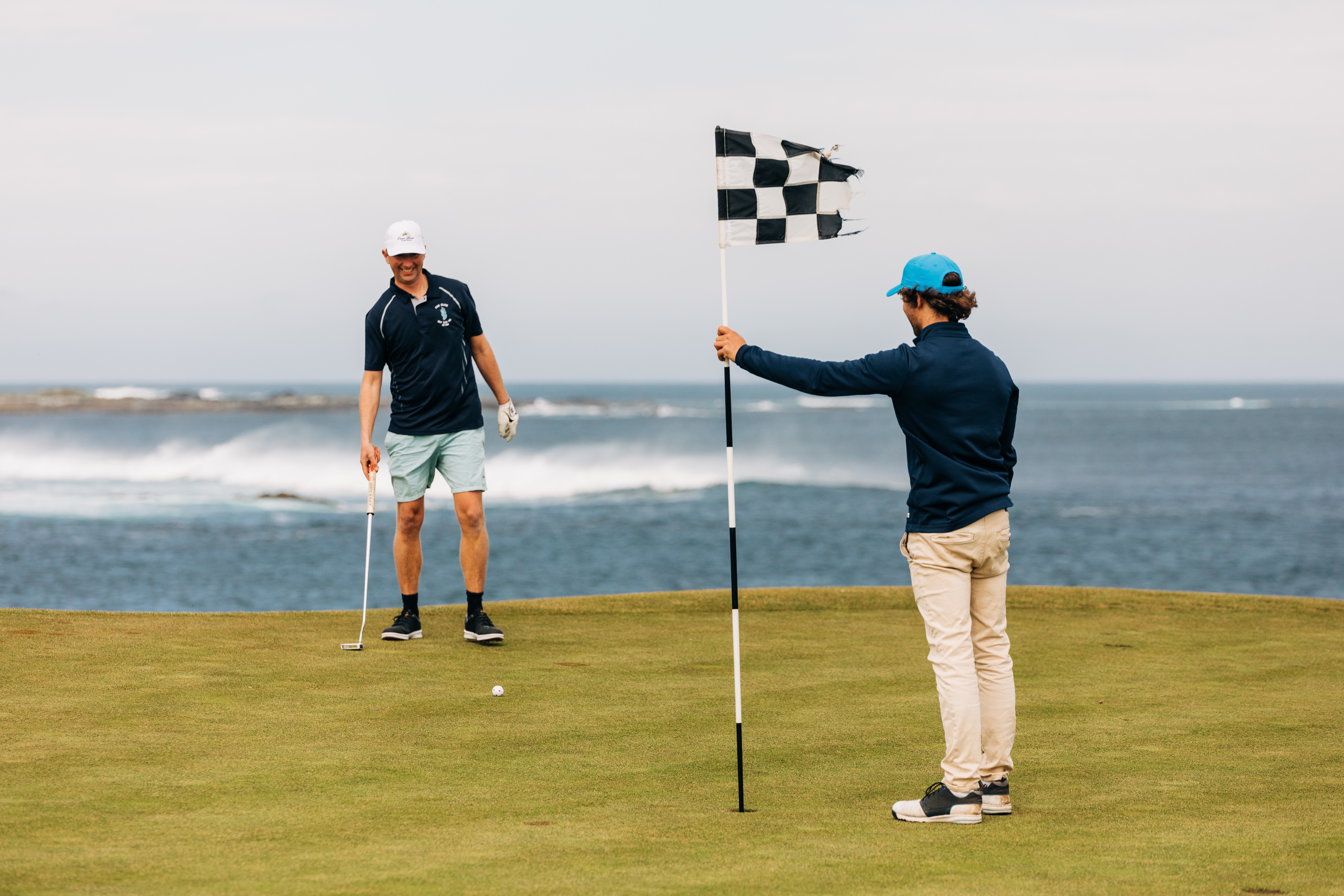 Golfers beside a black and white flag with the ocean behind them on King Island