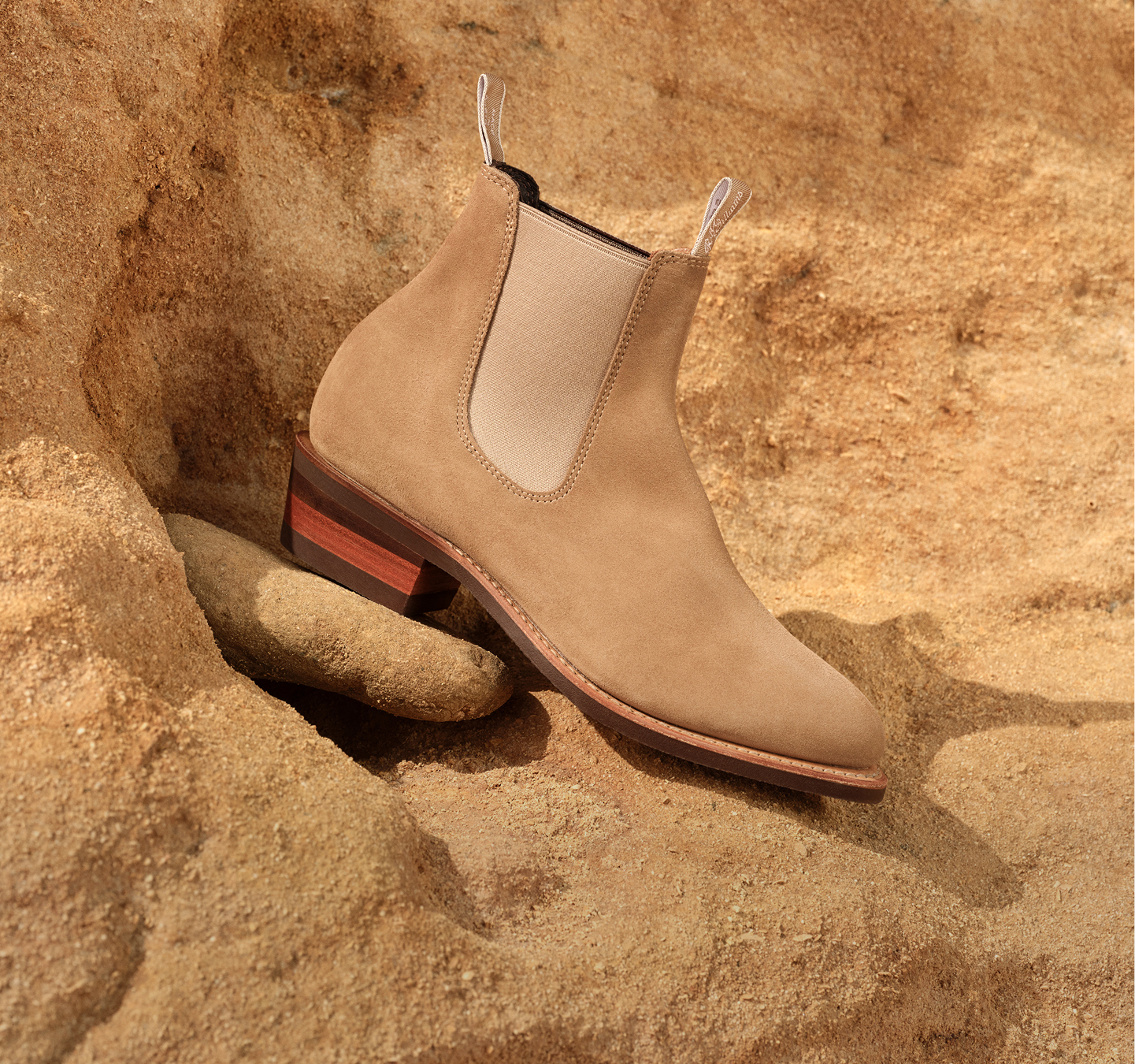 Close-up of a person’s feet in brown Chelsea boots, standing on a wooden surface with a grassy field in the background