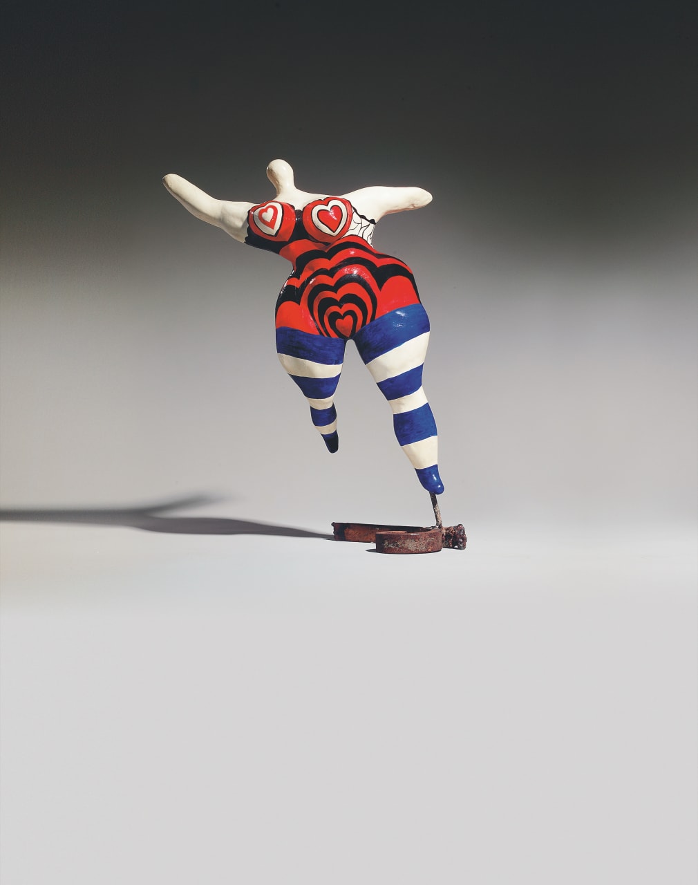 Small painted polyester sculpture of a dancing female figure with heart-shaped cups on her breasts and blue and white stripy tights