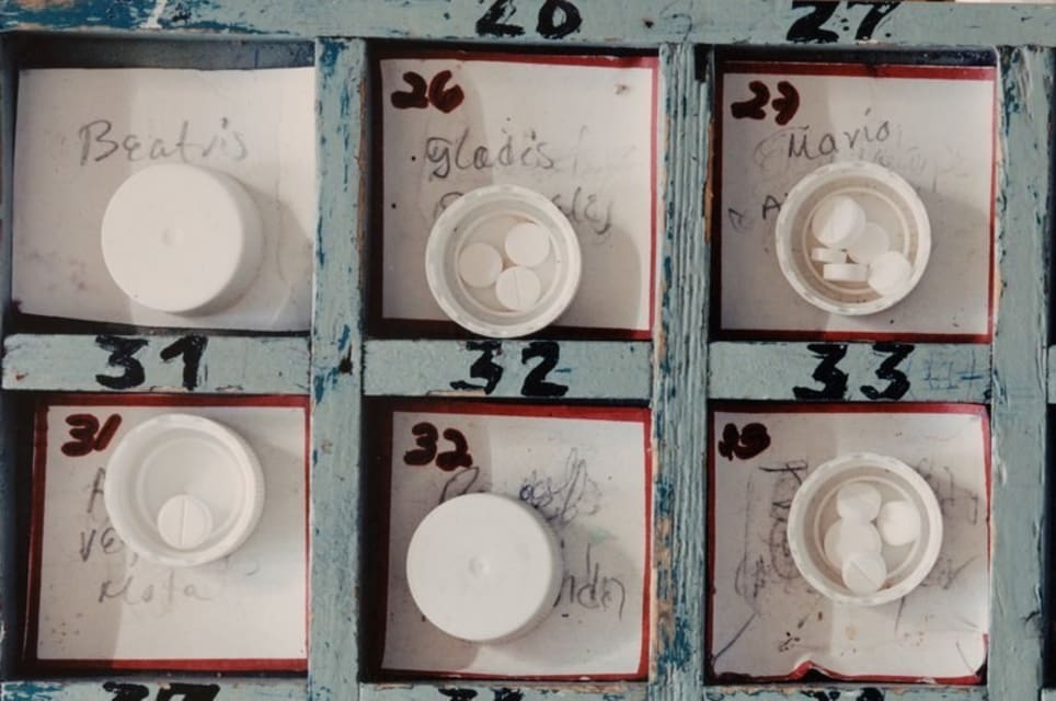 Photograph from above of 3x3 tray of numbered and named pots with medicine pills inside. Visible names are on the top row; Beatris, Gladis, Mario.