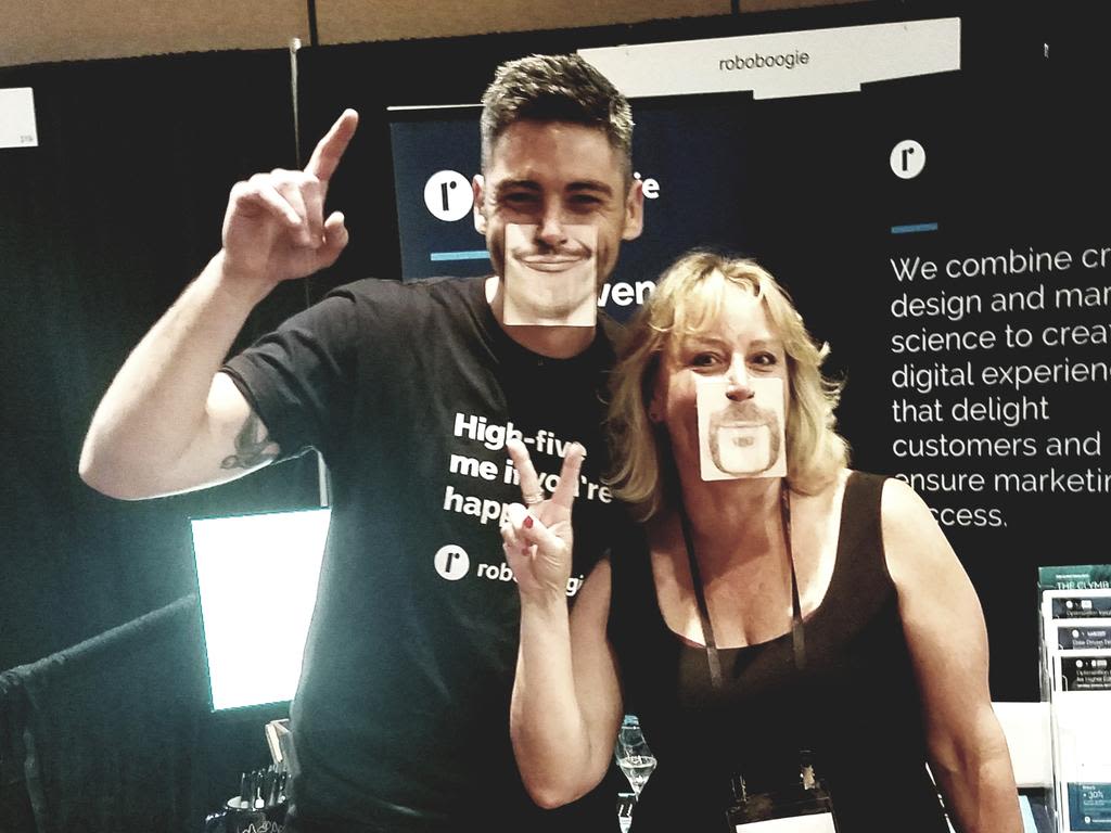 Two people smiling and wearing face coasters in front of the roboboogie booth
