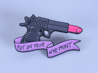 Pin esmaltado en forma de pistola con lápiz de labios y mensaje que dice "Ponte  ...