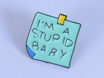 Pin esmaltado en forma de post-it, con la frase "Soy estúpido bebé"