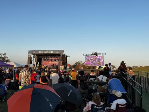 Festival crowd with umbrellas and tents facing the Entergy Stage and LED screen on the New Orleans Lakefront