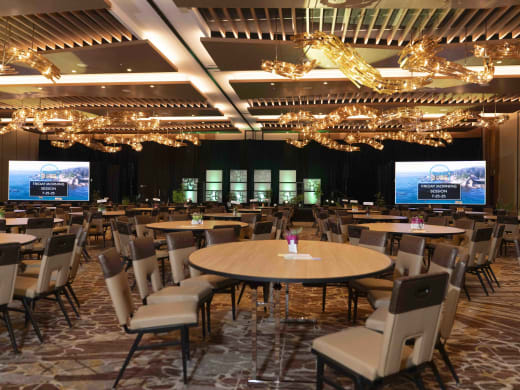 Purium ballroom set before doors with a center stage, two flanking LED screens, and round tables