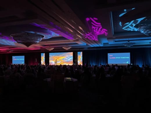 RAM Summit 2025 ballroom with magenta and blue patterns across the ceiling and session slides on the side screens