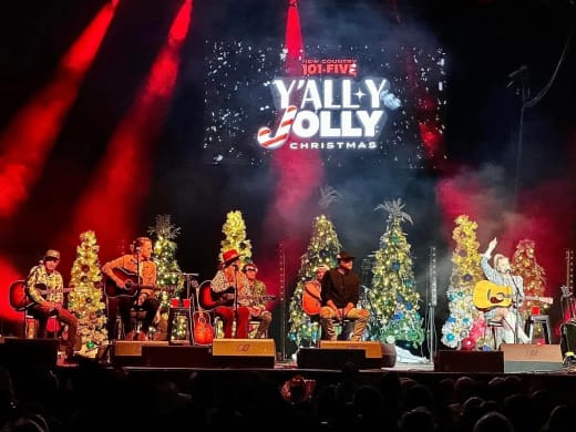 New Country 101.5 Y'all-y Jolly Christmas logo on the center LED screen above artists and Christmas trees, with red beams