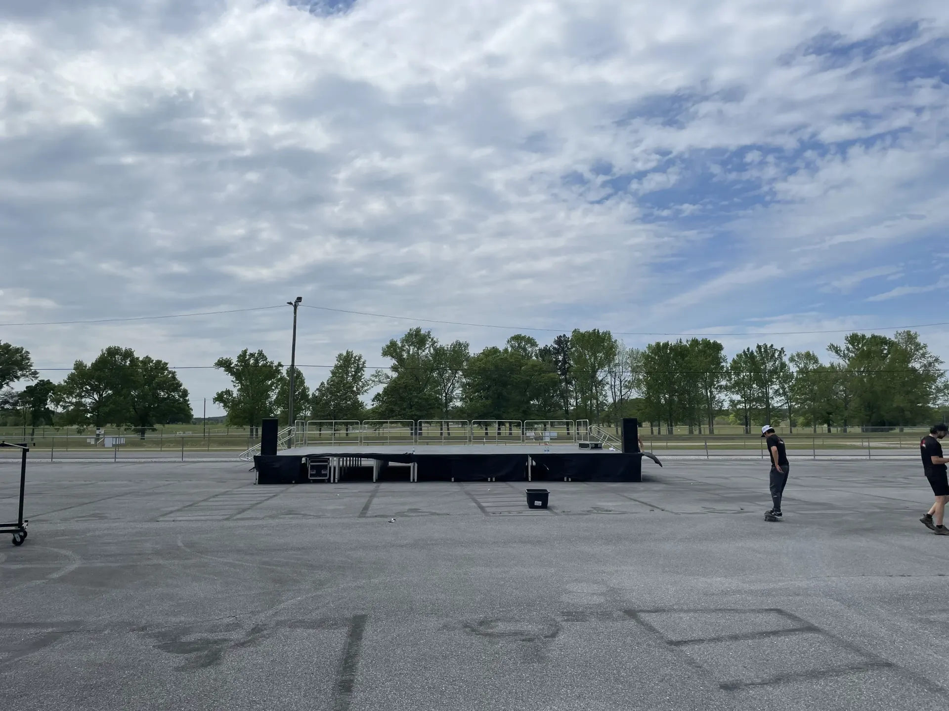 Large deck stage with safety rails and PA speakers set up in parking lot for outdoor event