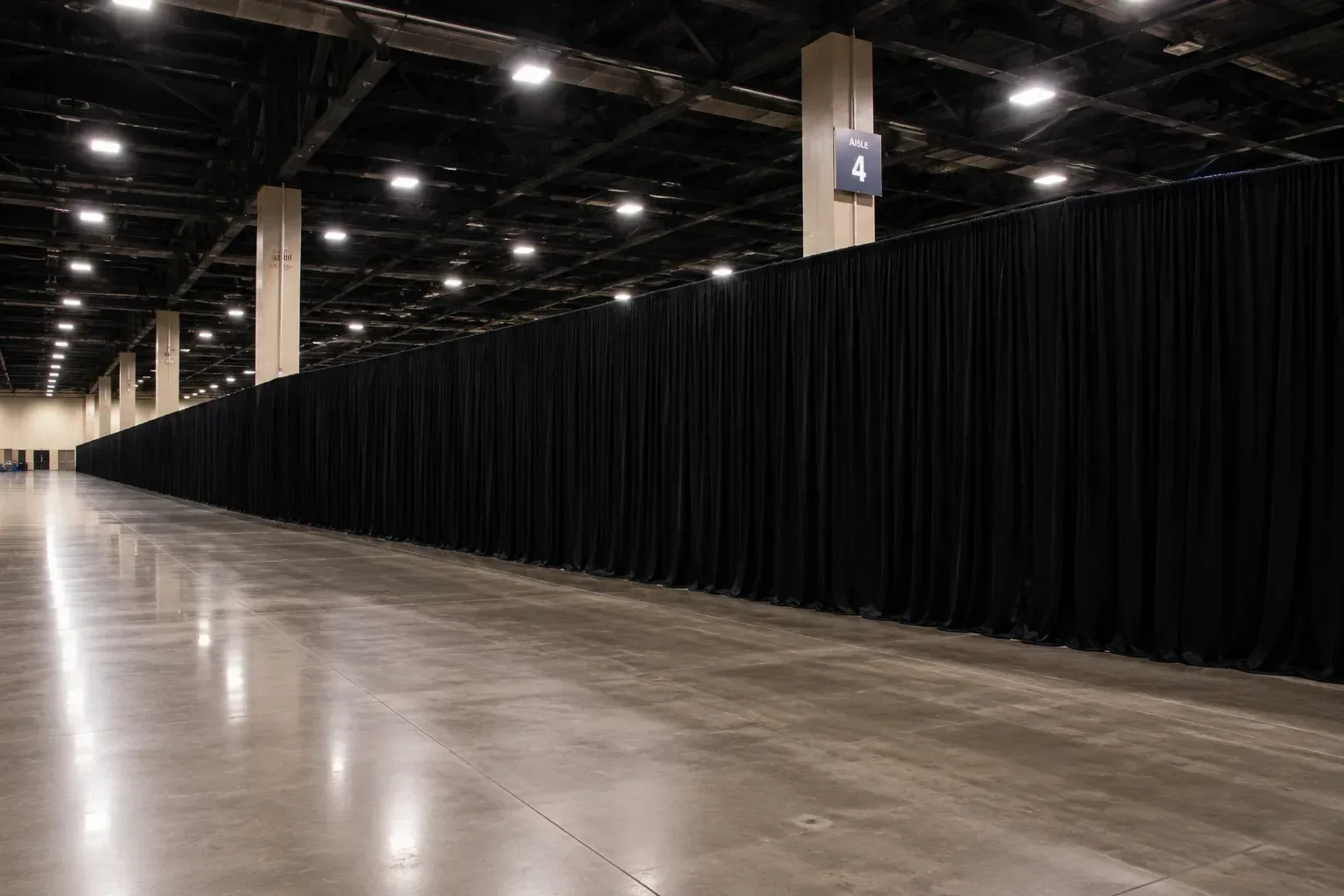 Long run of black pipe and drape masking the back of an empty convention center exhibit hall