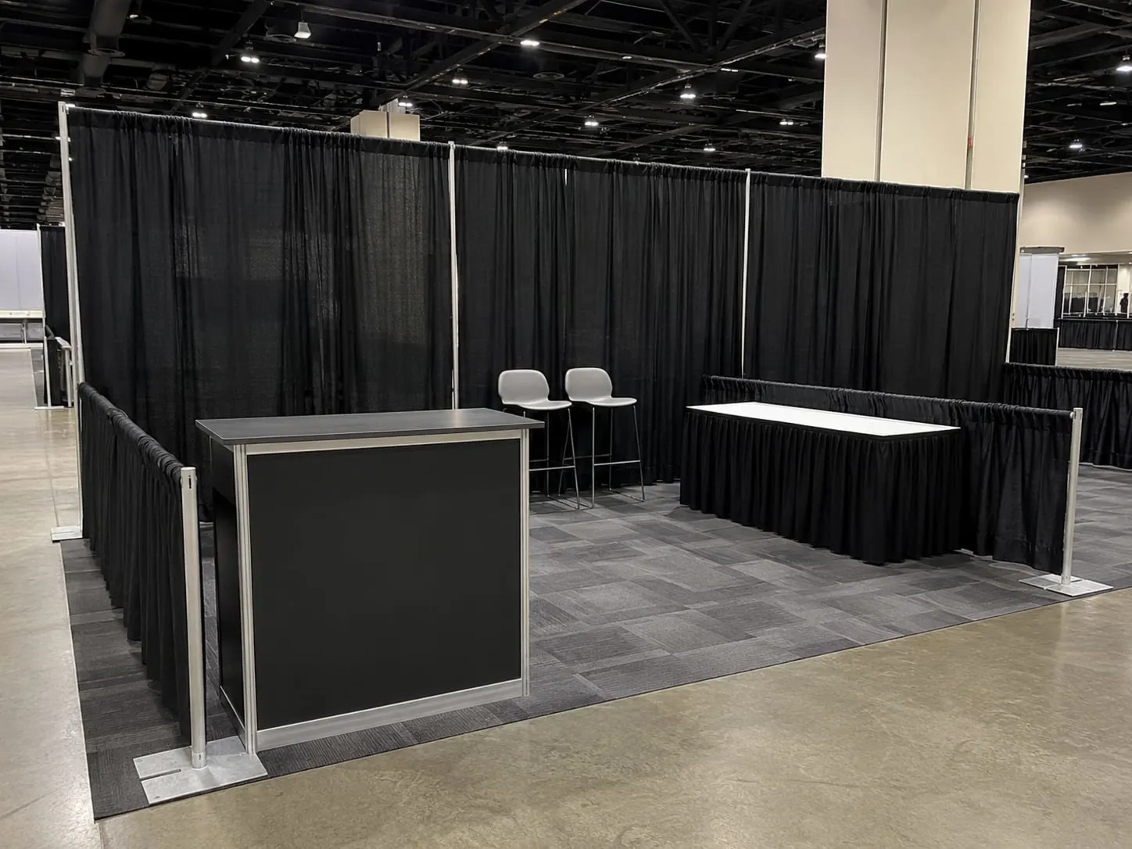 Trade show booth framed by an 8-foot black drape back wall and low side rails, with a counter and high-top table