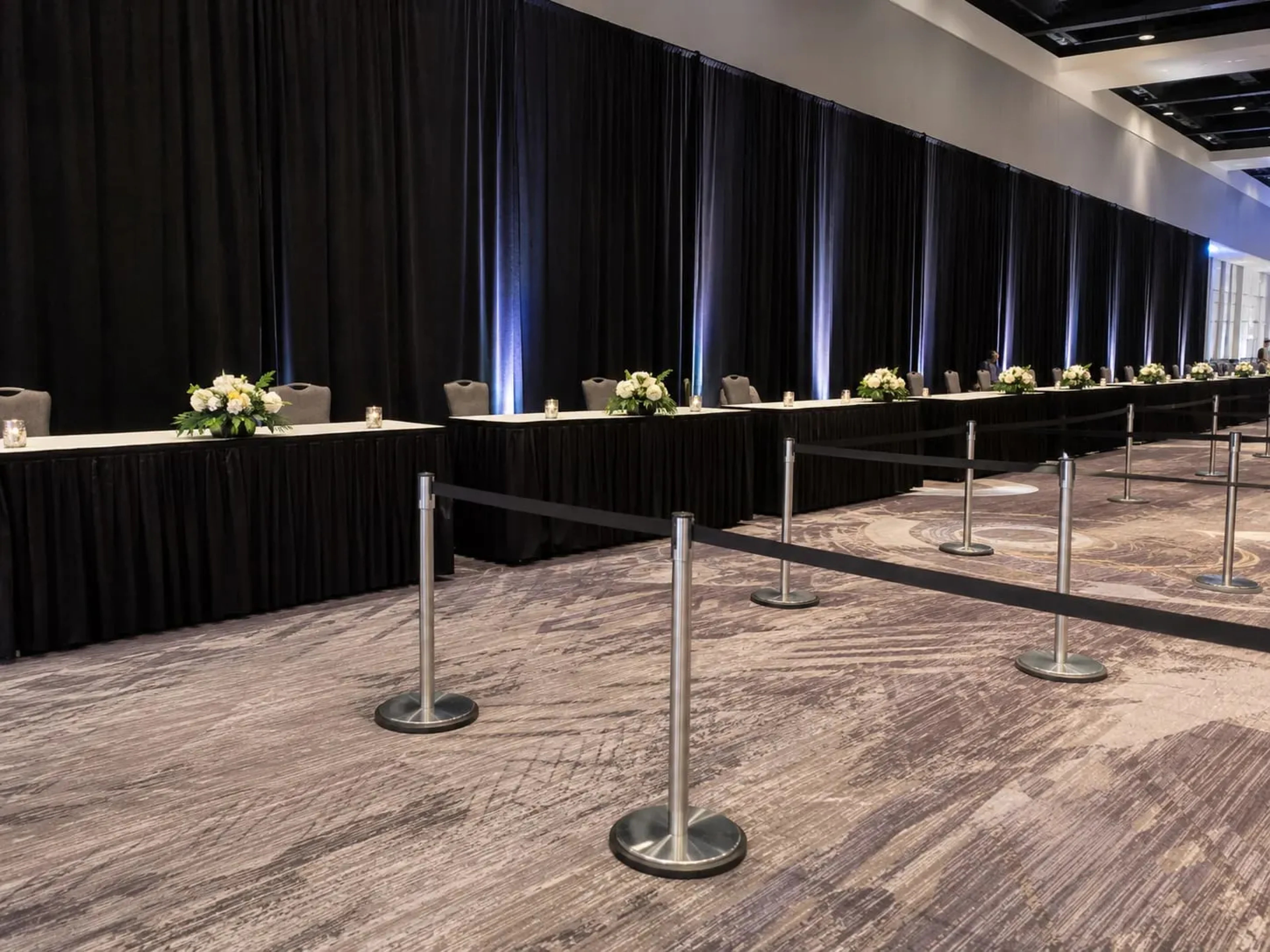 Long black pipe and drape wall dividing a hotel ballroom, with skirted tables and stanchions in front