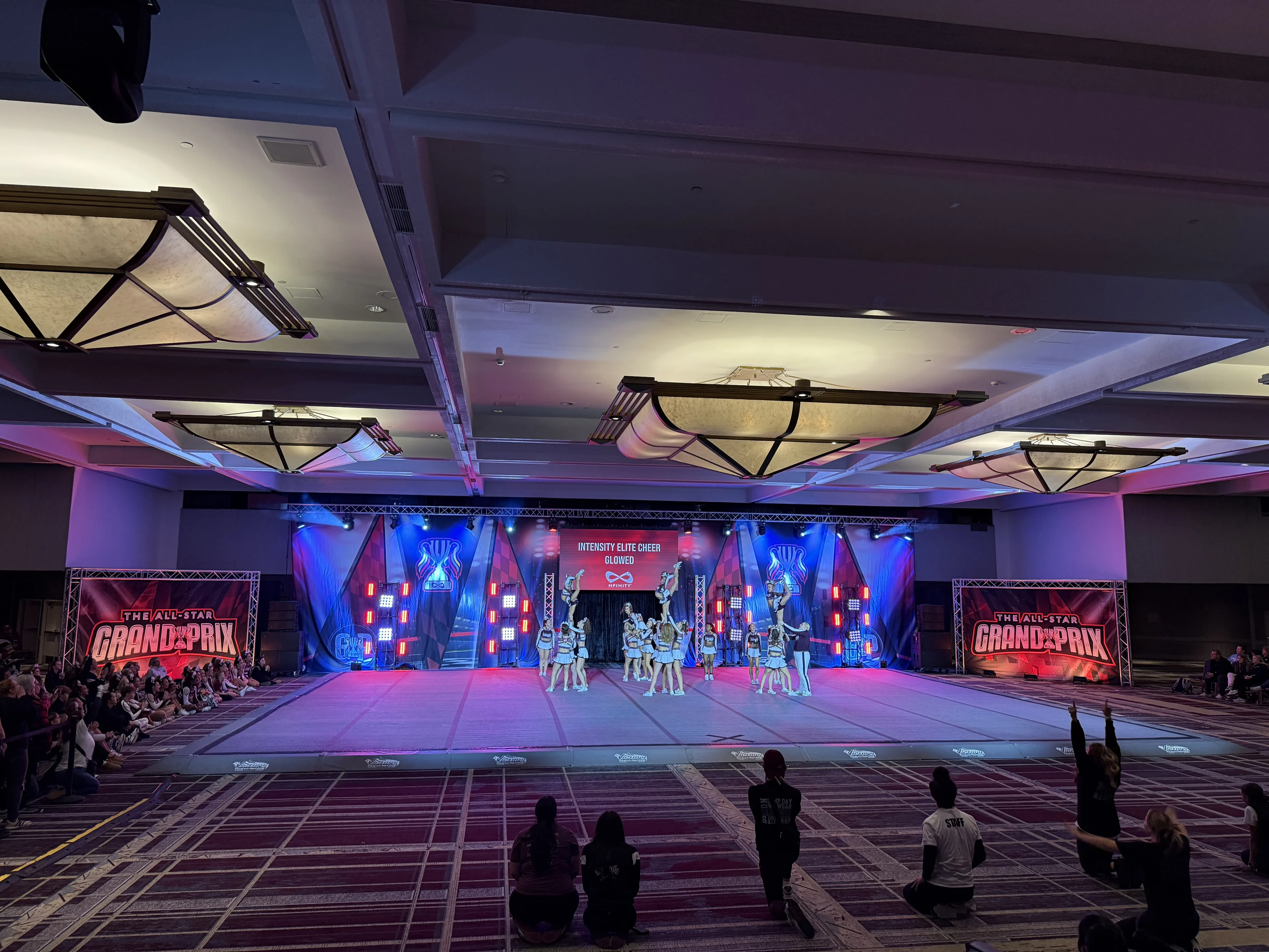 All-Star Grand Prix cheer competition on a ballroom performance mat with truss lighting, LED center screen, and red and blue wash