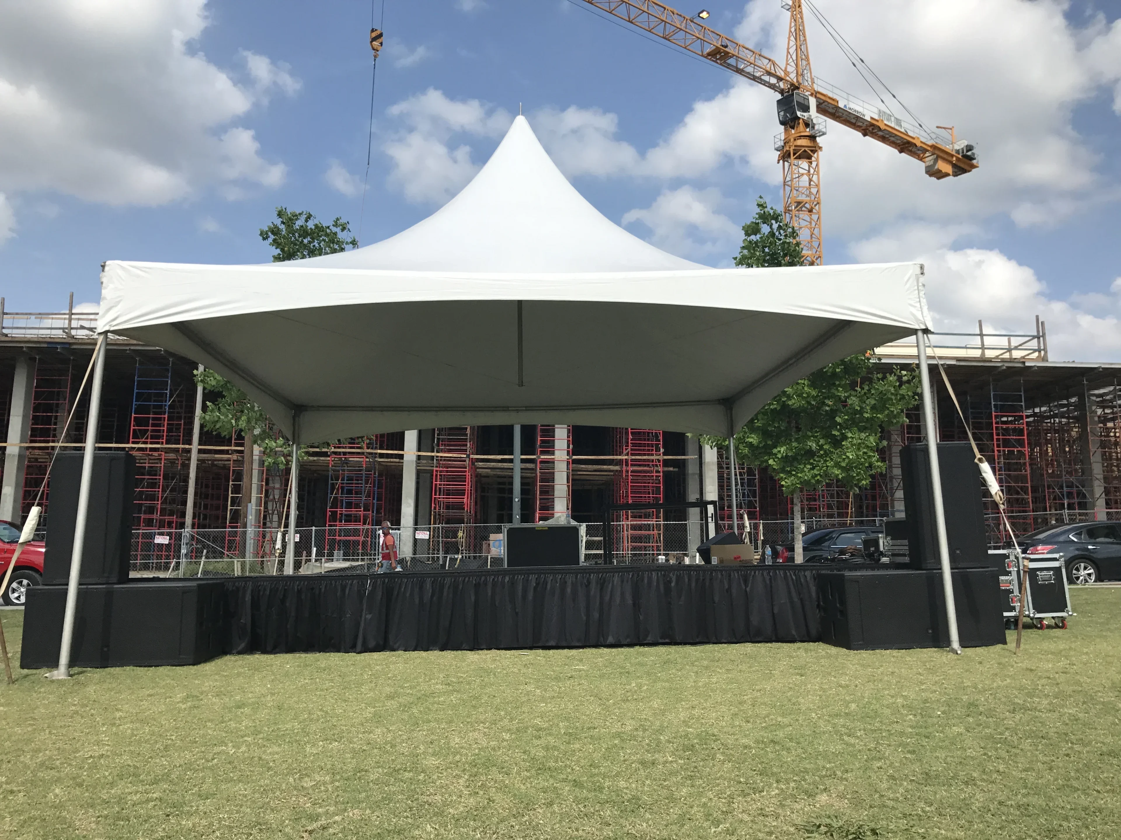 Skirted deck stage with PA speakers under a white peak tent on an outdoor lawn
