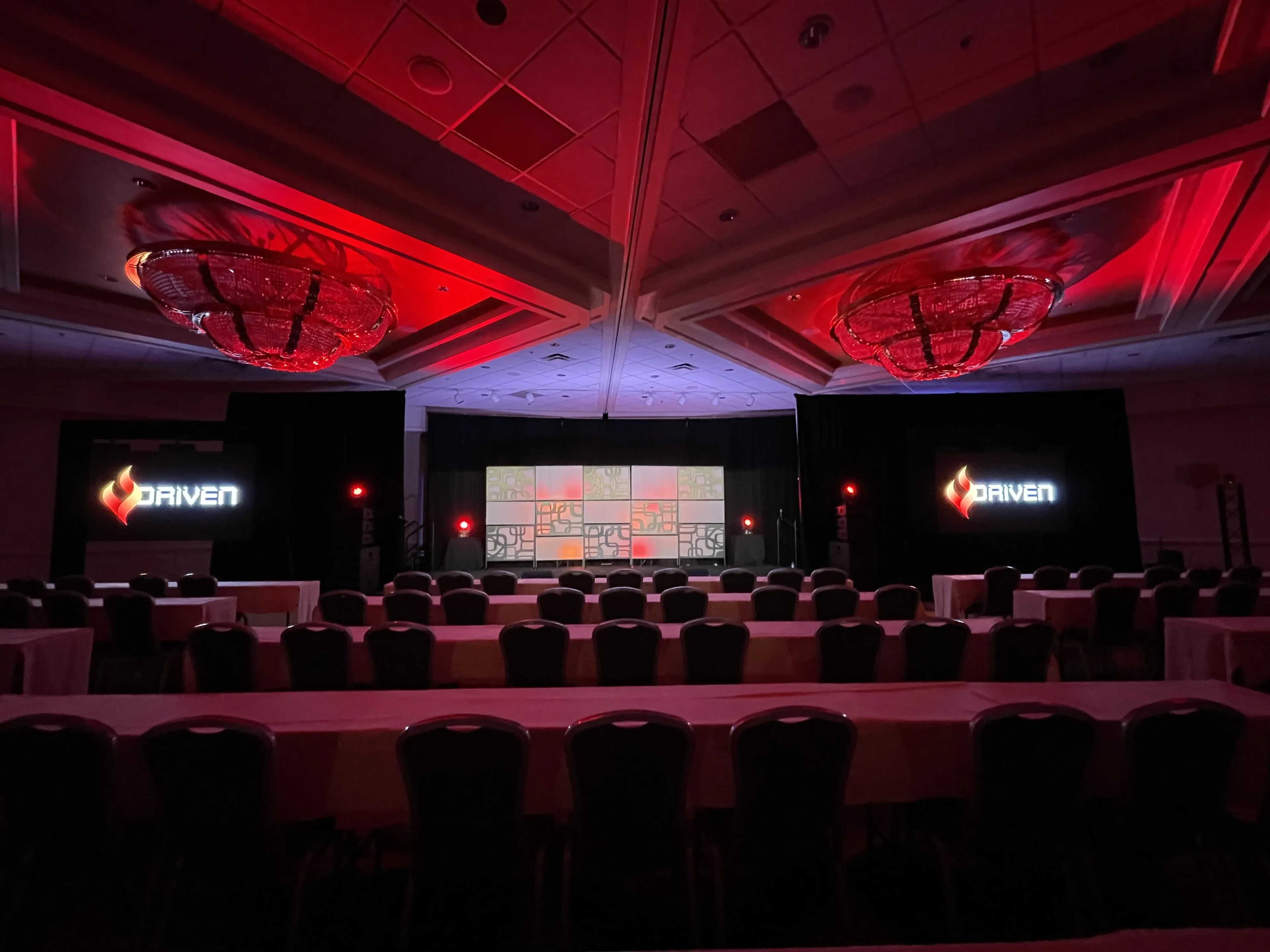 Driven corporate kickoff with dual side LED screens showing the Driven flame logo, decorative center LED set, banquet rounds and red ceiling-cove uplighting