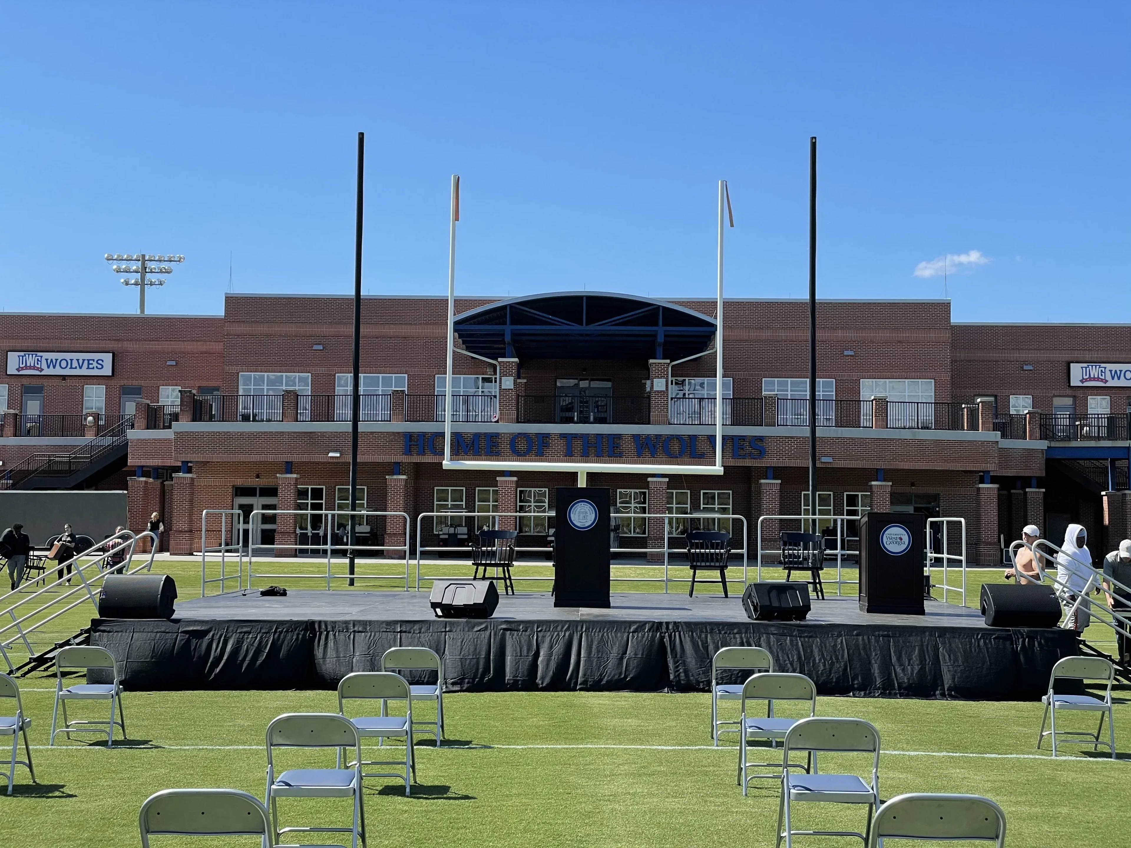 Skirted deck stage with podium and chairs set up on university football field for ceremony