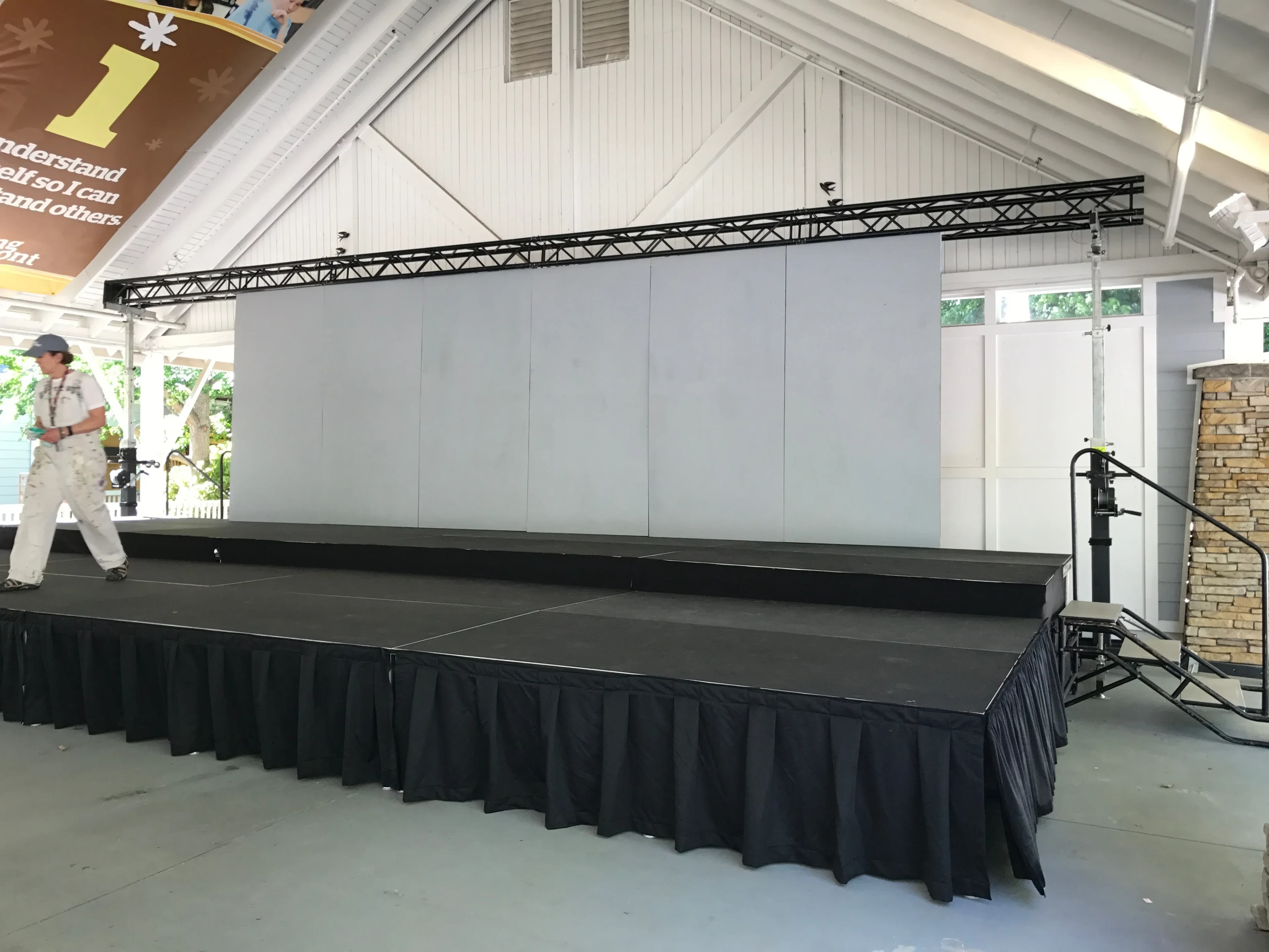 Skirted deck stage with backdrop wall and truss lighting under covered pavilion