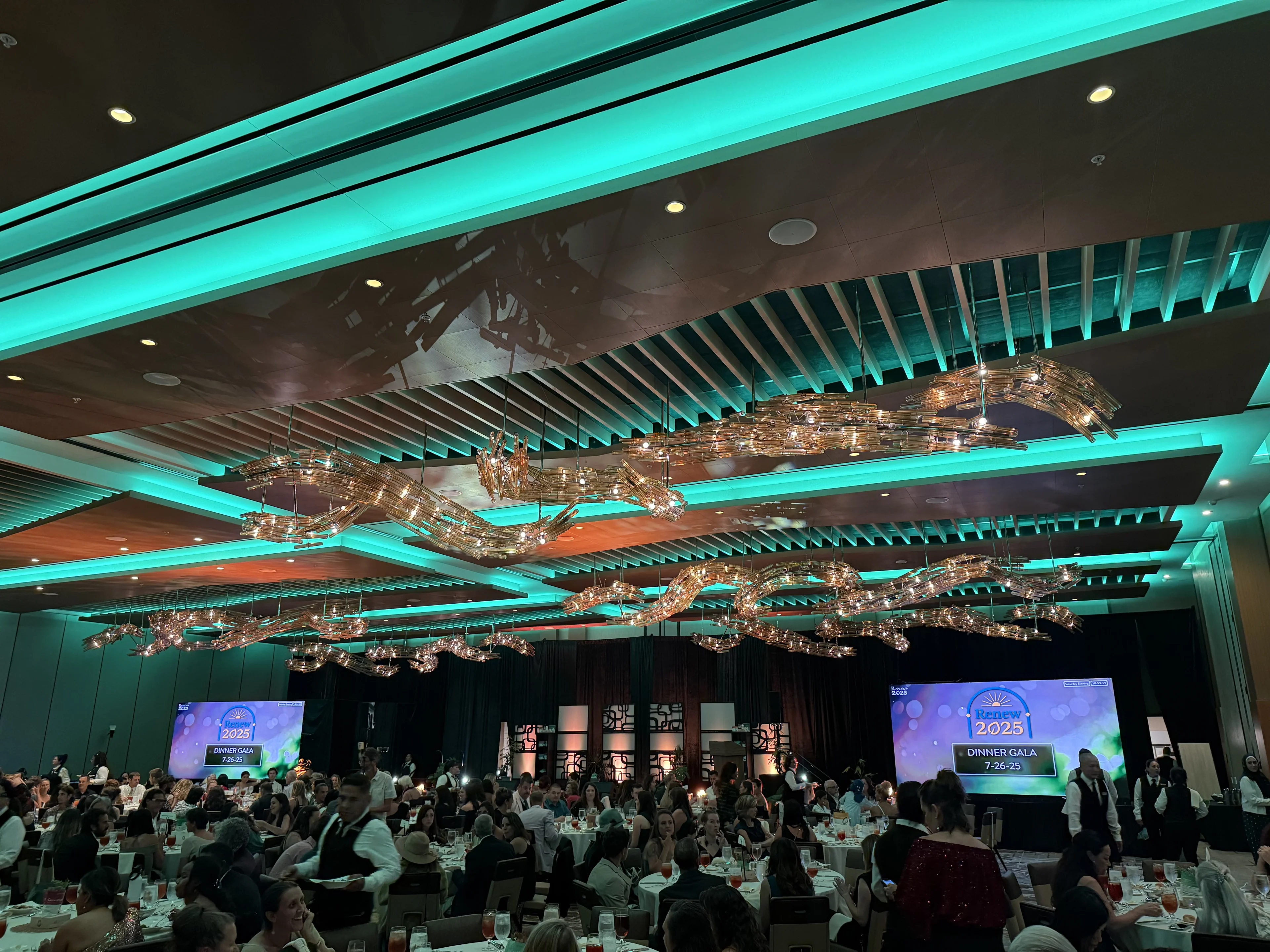 Packed dinner gala ballroom with LED screens showing event graphics