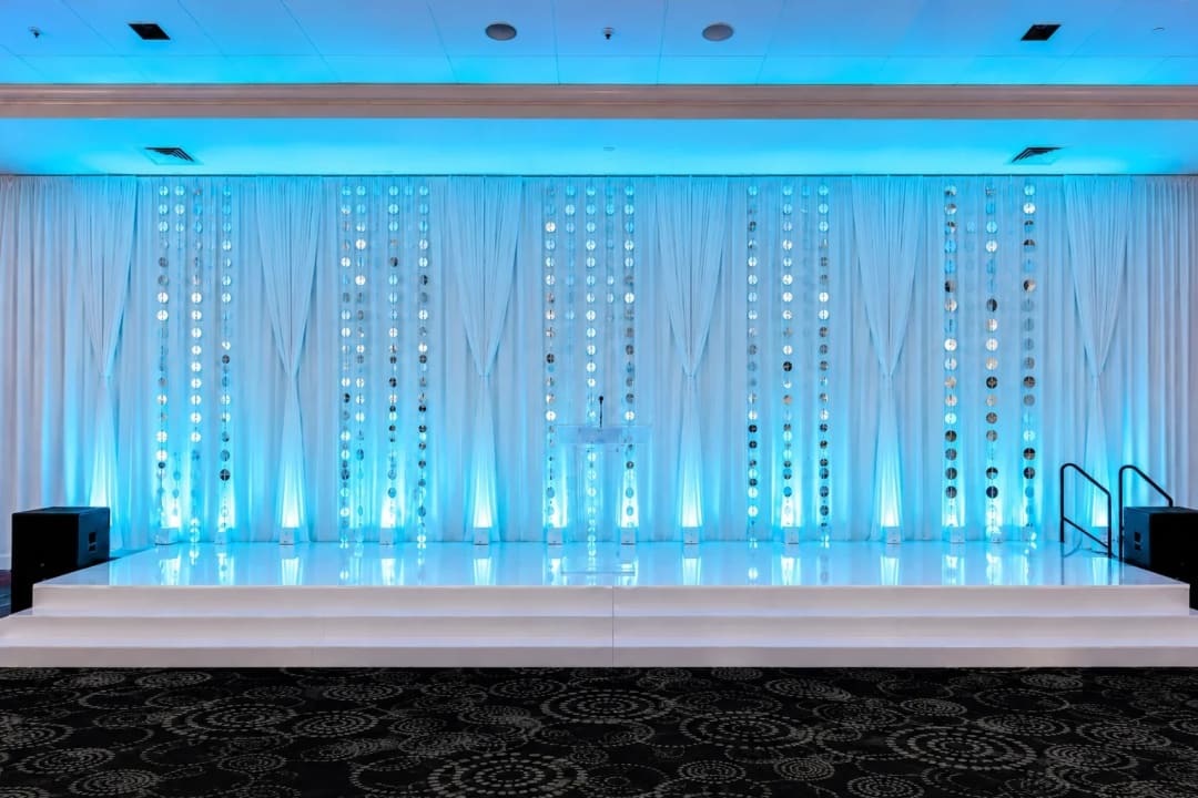 Teal-lit sheer backdrop with a beaded curtain behind a white stage at an Atlanta event.
