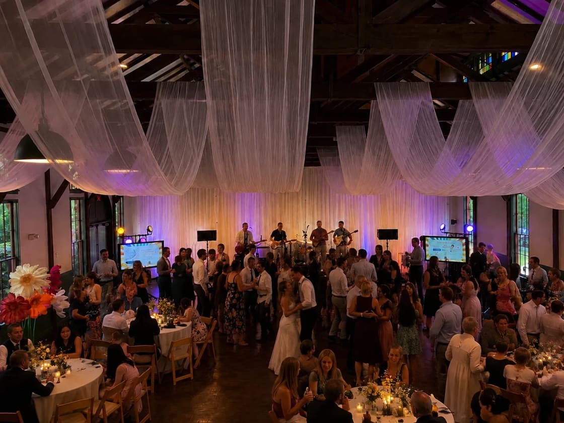 Sheer white ceiling drapery swagged across a timber reception hall above a full draped backdrop wall behind the band at an Atlanta wedding.