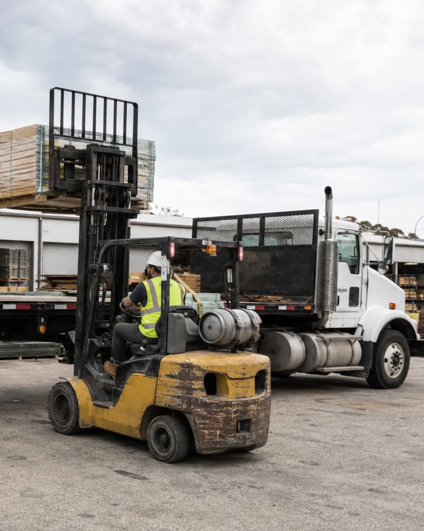A forklift lifting banded material onto a flatbed truck at a supply yard