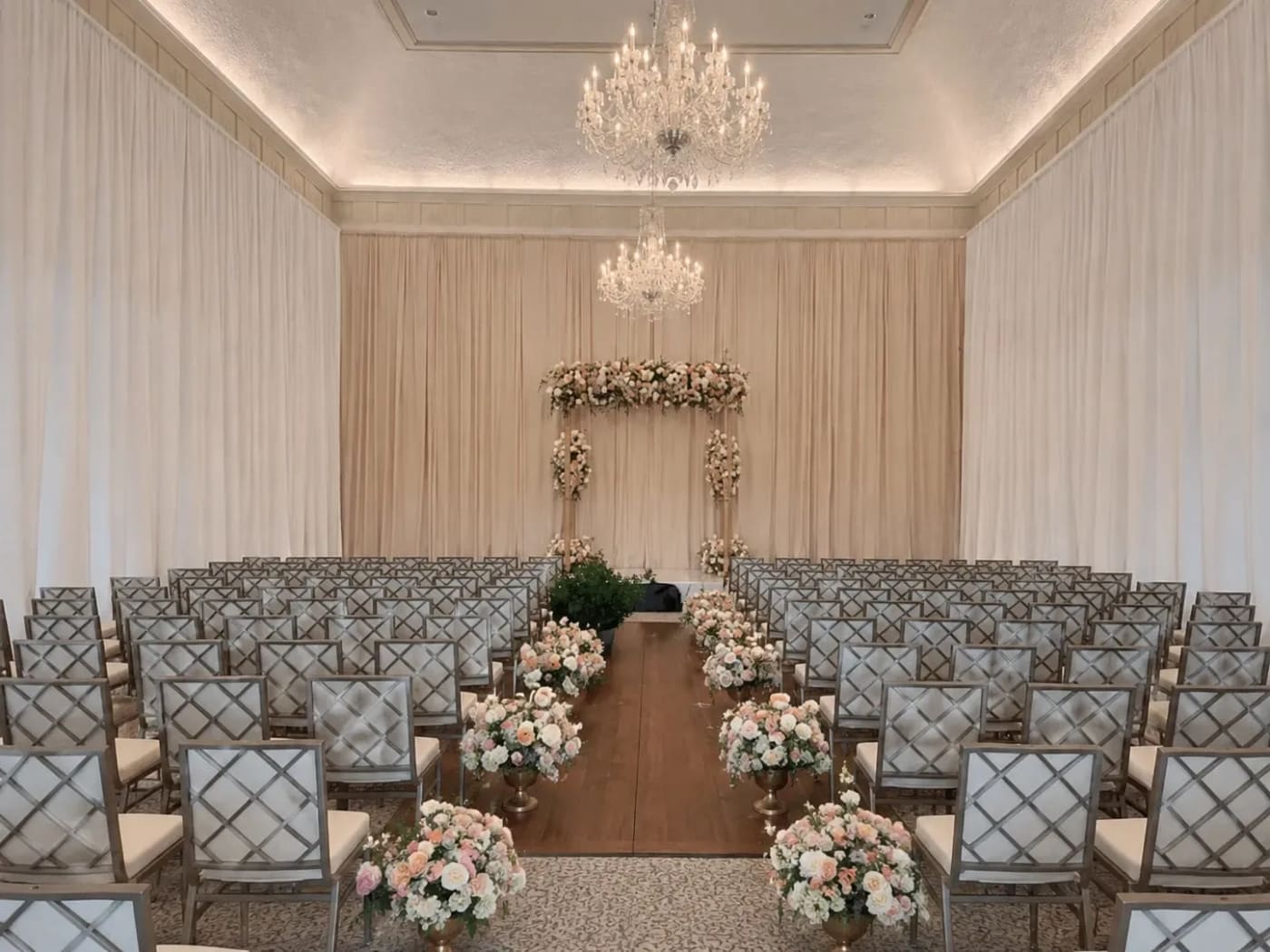 Elegant white wedding ceremony with a draped backdrop wall, chandelier, and floral-lined aisle at an Atlanta venue.