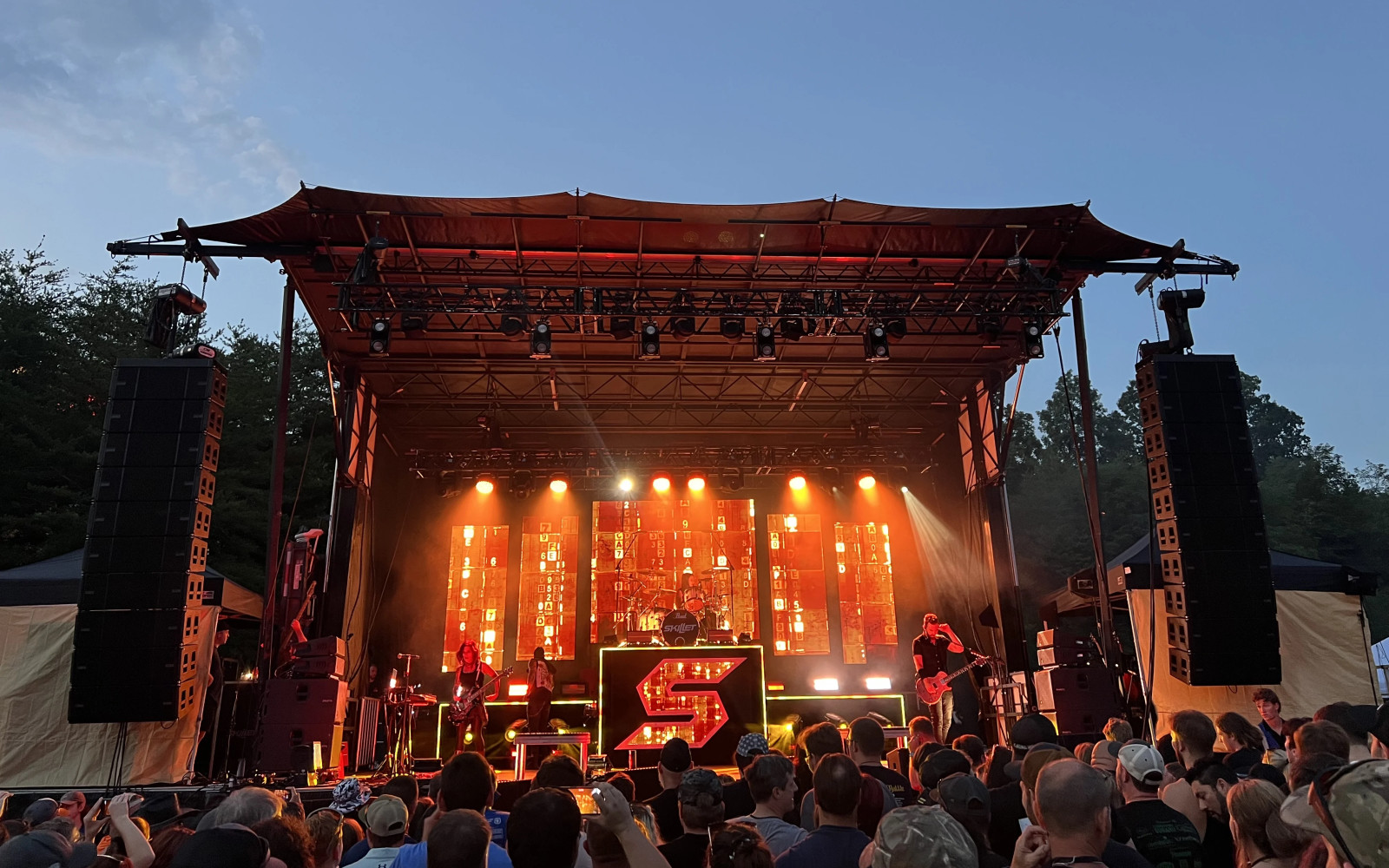Outdoor concert stage with LED wall backdrop, moving head beam lights on truss, and line array speakers