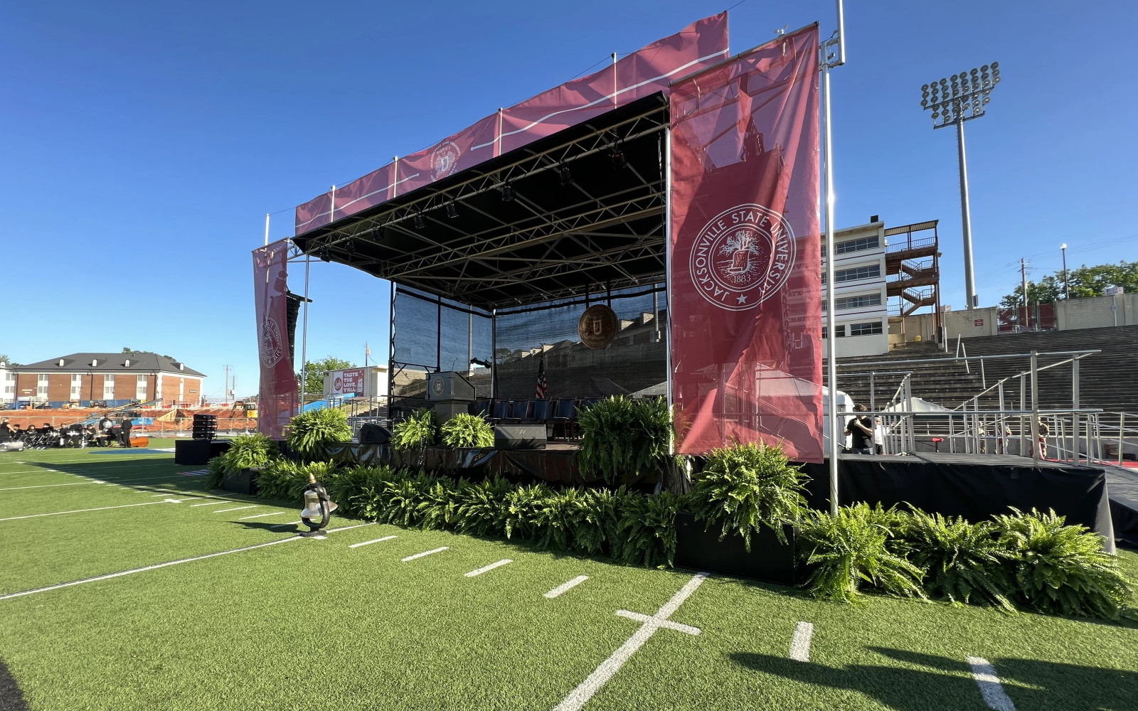 Jacksonville State University outdoor commencement stage with branded truss, platform, podium, and greenery
