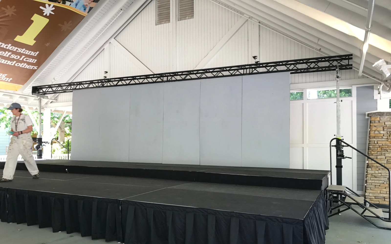 Skirted deck stage with backdrop wall and truss lighting under covered pavilion