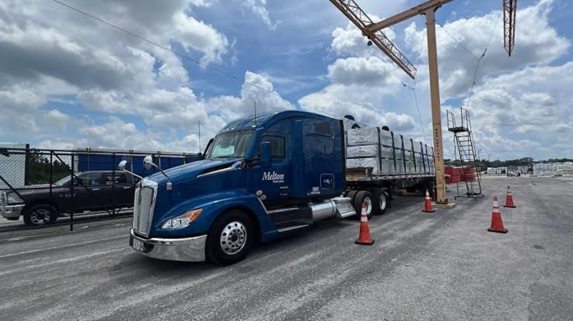 A tractor and flatbed loaded with construction material staged at a distribution yard