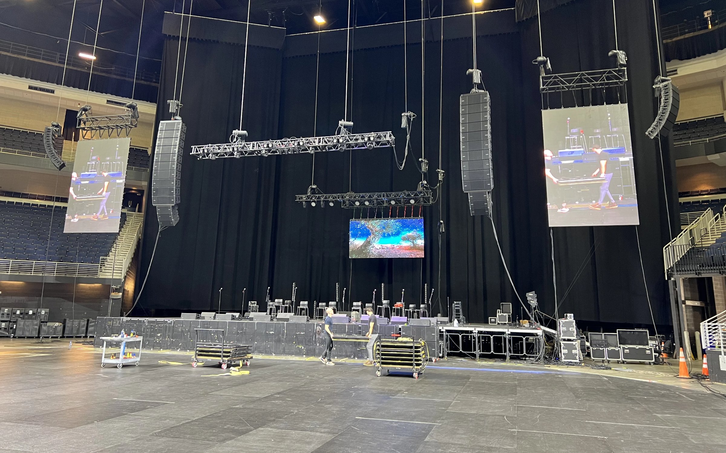 Arena concert load-in with multiple LED IMAG screens rigged from ceiling trusses