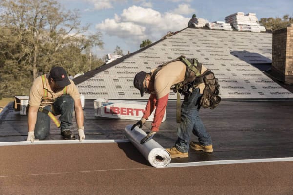 Roofers installing a Liberty SBS Self-Adhering Roof system rolling out a layer of the Liberty Cap Sheet. 