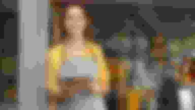 Female business owner in yellow shirt standing near a restaurant door.