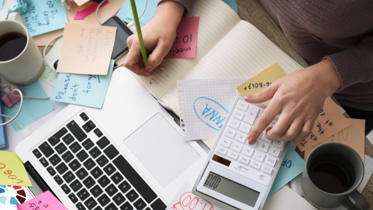 Accountant using a calculator on a very messy desk with lots of papers and post-it notes.