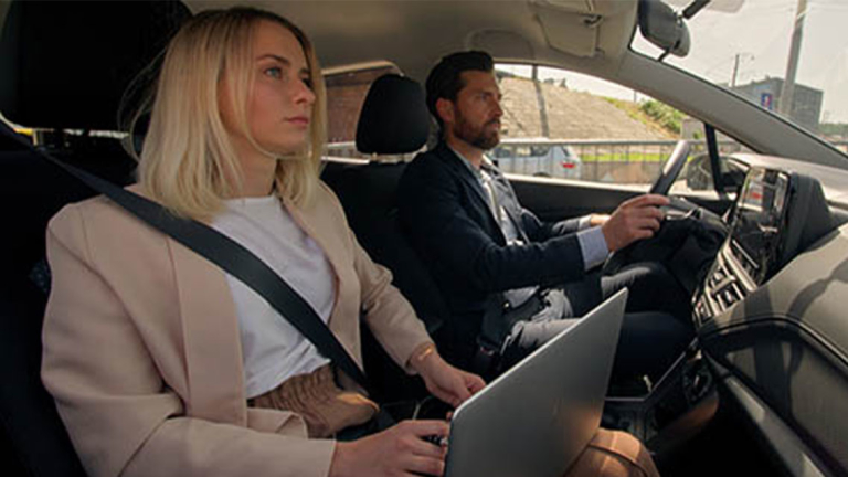 Two business professionals in a car, the passenger has her laptop open in her lap.