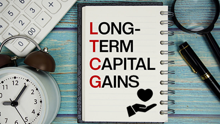 A spiral notebook, pen, magnifying glass, calculator and clock on wood.