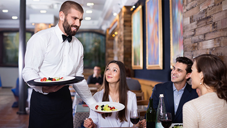 A waiter bringing food to a table in a restaurant.