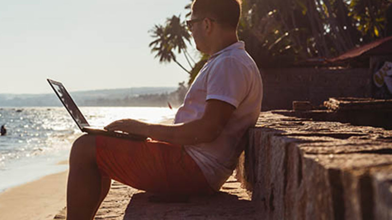 Man sitting on the beach with an open laptop.