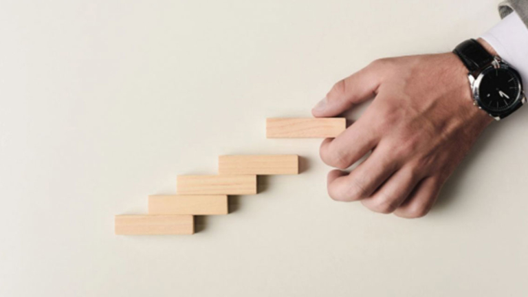 A man's hand stacking wooden blocks like stairs.