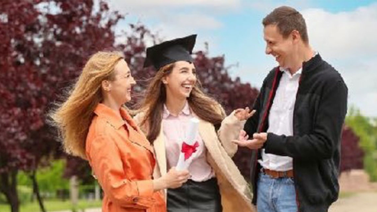 A student wearing a graduation cap with her parents on campus.