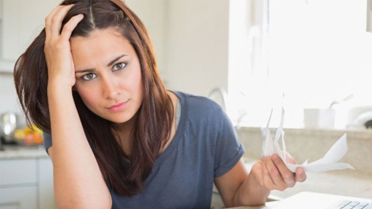 A woman holding receipts in one hand with her other hand on her head.
