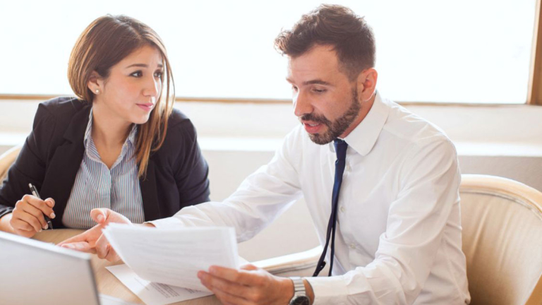 A man and woman at a table with an open laptop and papers.