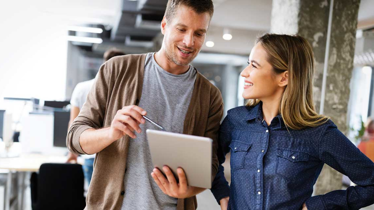 A man is pointing at a laptop with a pen while a woman smiles at him.
